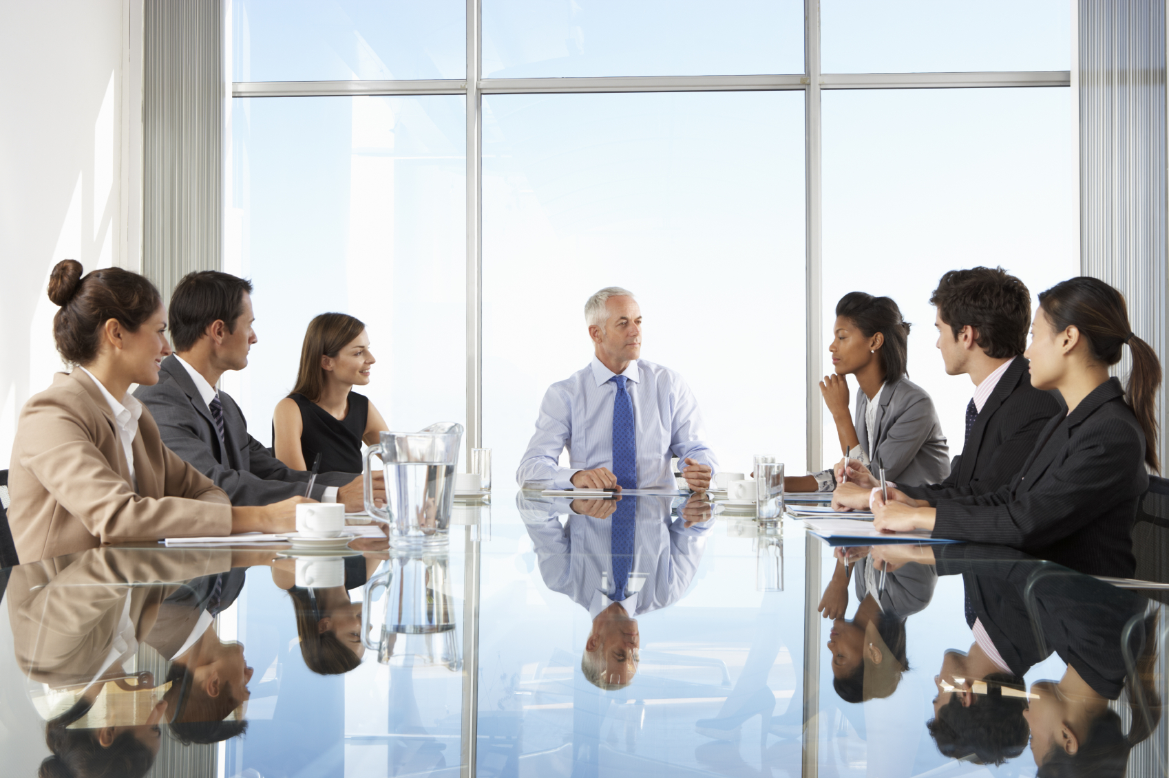 Group Of Business People Having Board Meeting Around Glass Table | Partners  by Design